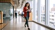 © Vasiliy - Businesswoman in red blazer walking through a modern office hallway using a tablet. Professional woman on the move in a bright corporate workplace. Productivity and technology concept