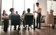 © Prostock-studio - Corporate Meeting Concept. Young Smiling Businessman Giving Speech During Meeting With Coworkers In Modern Office, Standing At Desk In Board Room, Explaining Strategy And Management