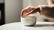 © Anna - A close-up shows a feminine hand in a cozy knit sleeve gently reaching toward a white bowl of warm soup on a round table in soft natural light.
