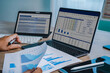 © onephoto - Hands reviewing financial chart document with laptop displaying spreadsheet dashboard and tablet screen, representing data analysis workflow, reporting process, business performance tracking, and digi