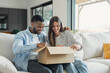 © Daniel - Happy young couple sits on a couch at home, smiling and opening a cardboard box together. Warm, relaxed moment conveying surprise, togetherness, new beginnings and home life.