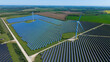 © AmazingAerialAgency - Aerial view of Chelveston Wind Farm featuring vast solar panel arrays and wind turbines across the green countryside in Wellingborough, England, United Kingdom.