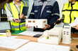 © Nuttapong punna - Engineer team in safety helmets discussing house model and blueprint. Construction planning, architecture design, project management