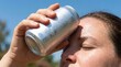 © iri.madrid.art - Close-up of woman cooling her forehead with a cold aluminum can on a hot summer day for wellness and refreshment background or banner