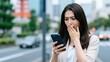 © CrazyJuke - Shocking News on Mobile: An Asian woman in surprise looks at her smartphone screen. Expressing a mix of surprise and concern in an urban setting.