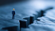 © sam richter - A lone miniature business figure stands precisely on the edge of a vast, deep blue canyon crack, representing concepts of risk and decision.