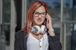 © tetxu - Businesswoman with headphones and phone in front of building
