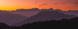 © PATMALUPHOTO - Layered mountain range and forest silhouettes against a vibrant orange sunset sky, showcasing a tranquil alpine travel destination. Brenta Dolomites from Paganella plateau, Trentino, Italy.