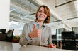 © BusinessClass by W61 - Businesswoman showing thumbs up and smiling in modern office