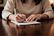 © Maryna - Person writing on document paper with pen at table. Focused individual completes task indoors. Warm light creates calm mood. Focus on hands and writing.