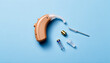 © Alex & M Studio - Modern behind the ear hearing aid with a small battery and cleaning brush isolated on a light blue background representing elderly healthcare medical assistance and audiology tech