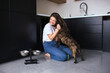© Vlad - Young woman in kitchen during quarantine. Girl playing with her french bulldog puppy. Dog licking woman's cheek. Together in kitchen.