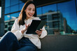 © BullRun - Young woman using smartphone sitting on yellow bench at bus stop, browsing digital content, mobile application, urban commute, wireless 5G connection, lifestyle photography, city background.