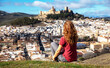 © M.studio - young woman sitting on a hill and contemplating the panoramic view of alcala la real and the historic fortress of la mota, spain