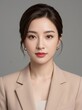 © JetHuynh - This professional studio portrait features a confident young woman wearing a beige blazer with dark hair styled in an updo against a neutral gray background