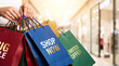 © Aurora Aesthetics - shopping big sale shop now limited offer paper bags mall promotion discount retail bright close up of female hand holding bunch of red blue green packets with text in modern shopping center hallway