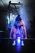 © ultramansk - A powerful athletic woman performing a heavy barbell lift amidst dramatic blue neon lighting and mysterious smoke effects in a modern low-light fitness studio.