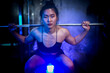 © ultramansk - A strong woman performing a barbell squat with atmospheric smoke and dramatic blue lighting in a high-end modern gym facility.