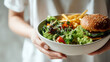 © KotBaton - Bowl with salad and burger with fries, mixed meal concept combining healthy and fast food elements.