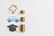 © ngstock - Finance investment concepts paper house car and graduation cap cutouts arranged beside coin stacks on white surface