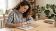 © kodidesign - Young woman with curly hair drawing a pencil portrait in a home studio. Creative freelance artist working on a commission at a wooden desk
