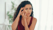 © Prostock-studio - A woman with curly hair shows concern while touching her face. She sits in a well-lit room with indoor plants visible. The expression on her face suggests she is feeling anxious or troubled.