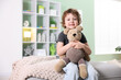 © New Africa - Smiling little boy hugging plush toy bear on pouf at home. Space for text