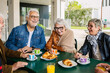 © Xavier Lorenzo - Senior people sitting at an outdoor table, laughing and enjoying breakfast with pastries, coffee, and juice, sharing moments of friendship and happiness