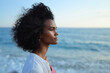 © SISMIZ - Serene woman with curly hair gazes thoughtfully at the ocean horizon