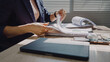 © WARAPHON - Woman flips through documents at desk. Natural light filters through blinds behind her. Focused, she organizes paperwork with care. Closed laptop rests nearby, ready for use
