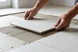 © Netsai - Hands of a skilled worker meticulously placing a light-colored tile onto a floor with fresh adhesive during home renovation.