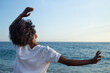 © SISMIZ - Woman with curly hair embracing the ocean breeze with open arms