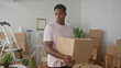 © Krakenimages.com - Man holding cardboard box, hands gripping edges while looking aside inside a packed apartment building; moving day reflective.