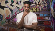 © Krakenimages.com - Man with hand to chin and folded arm standing on street stairway covered in graffiti; thoughtful introspection.