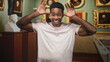 © Krakenimages.com - African american man grinning with hands raised, fingers splayed and tongue out while standing before framed portraits and classical busts in a gallery building; playful joy and curiosity.
