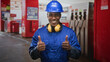 © Krakenimages.com - Man wearing blue hardhat and yellow earmuffs with arms crossed smiling at gas station building; confidence teamwork reliability.