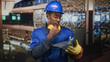 © Krakenimages.com - Man in hardhat wearing blue coverall and noise cancel headphones holding laptop with wrench and hand to chin in building; focused problem solving.