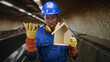 © Krakenimages.com - Man builder wearing blue hardhat and yellow ear protectors holding a small wooden house while raising a gloved hand in building; pride duty.