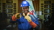 © Krakenimages.com - Man in hardhat holding cuban flag, wearing yellow gloves and earmuffs, smiling while pointing finger toward camera in building; national pride.