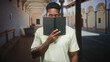 © Krakenimages.com - Man peeks over book with hand covering lower face in an arched building corridor; curiosity study focus.