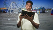 © Krakenimages.com - Man holding a black book, hands visible and mouth open in surprise at a street fair with a ferris wheel and amusement booths; surprise curiosity.