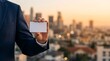 © Bangga - Blank white card held by a businessman in a navy suit against a warm golden hour city bokeh. Sharp focus on the card. Ideal for corporate contact and identity marketing.