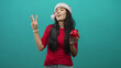 © Krakenimages.com - Young woman wearing santa hat holds red piggy bank and shows peace sign in studio; festive savings cheer.