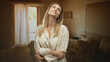 © Krakenimages.com - Woman smiling and looking up, arms folded across waist beside a curtain and unmade bed in a building; serenity reflection.