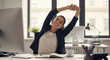 © Febi - Happy Young Businesswoman in Black Blazer and White Blouse Stretching with Arms Overhead at a Modern Office Desk with Computers and White Coffee Cup