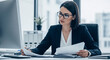 © Febi - Serious professional businesswoman in a dark suit with glasses working with documents at her desk in a modern office environment
