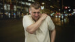 © Krakenimages.com - Man clutching his shoulder and grimacing on a busy city street at night under streetlights and blurred cars; pain.