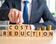 © magele-picture - Cost reduction - Geschäftsmann zeigt auf den Text 'Cost reduction'