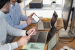 © Studio Marmellata - Two men collaborate at a desk, analyzing financial data on a smartphone and laptops, discussing business strategy in a modern office environment.