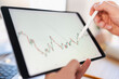 © Studio Marmellata - A person uses a stylus to interact with a financial chart displayed on a tablet, analyzing market trends and data.